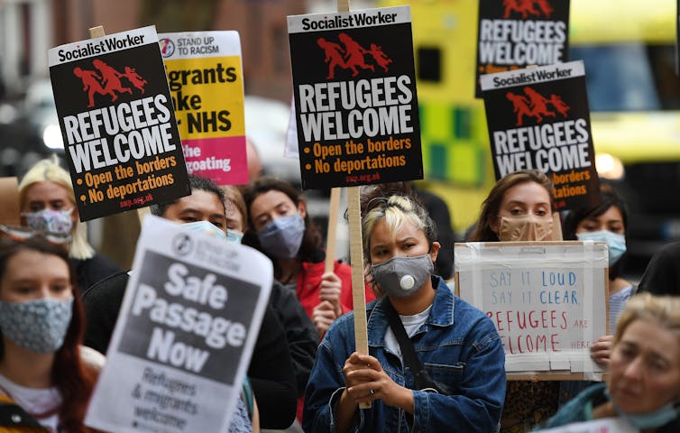 Protesters against the UK's asylum policy wearing facemasks and holding placards demanding safe passage for refugees.