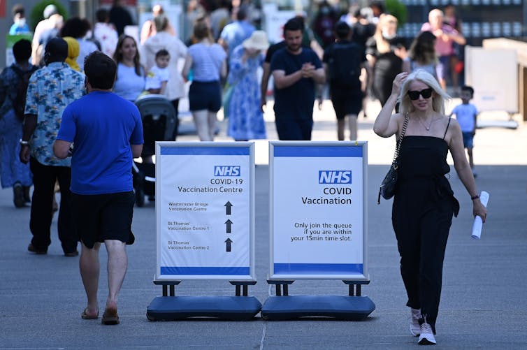 People walking past signs at the entrance to a COVID-19 vaccination centre