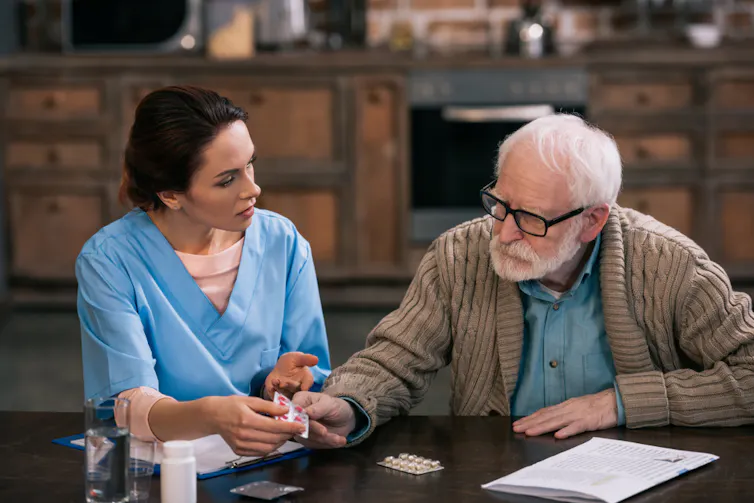 A young nurse sitting with an elderly patient discussing medication.