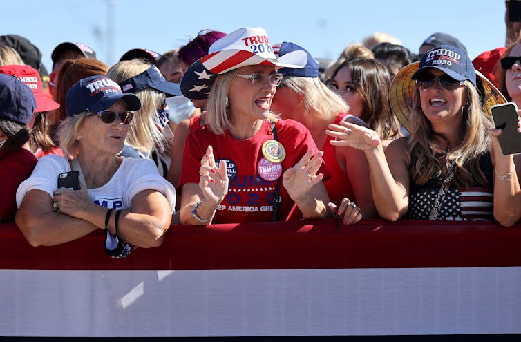 Three middle-aged women at a rally wearing Trump hats.