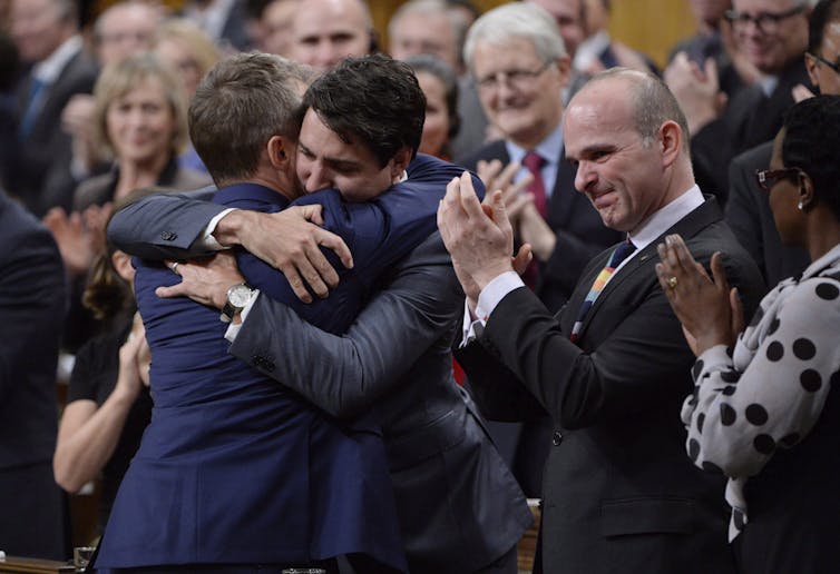 Justin Trudeau hugs a man while others clap in the background