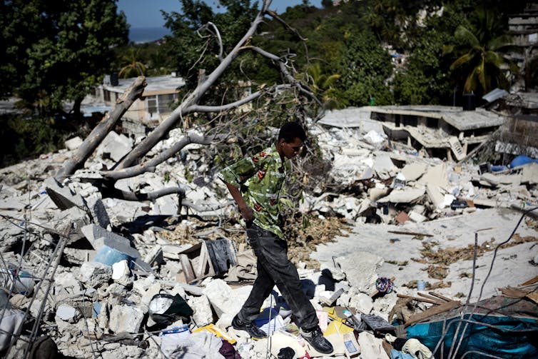 A man walks over the remains of several homes where bodies of earthquake victims had yet to be pulled from the rubble.