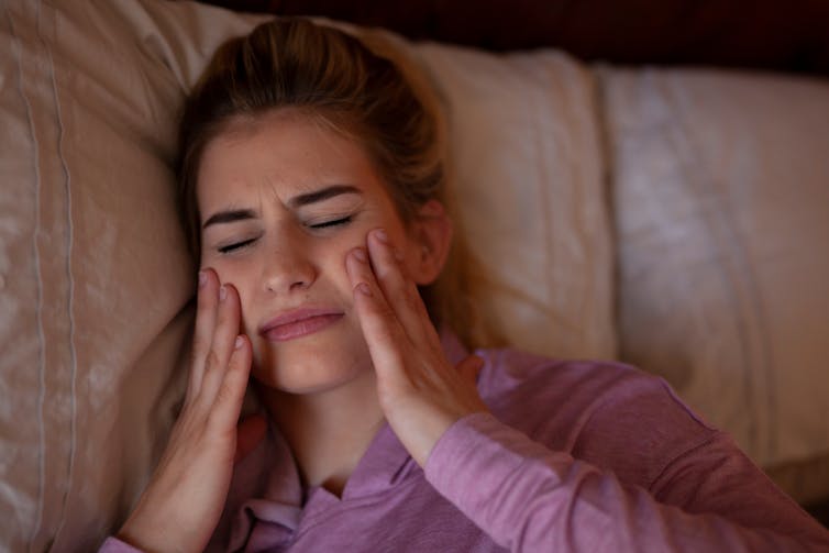 A young woman in bed holds her cheeks