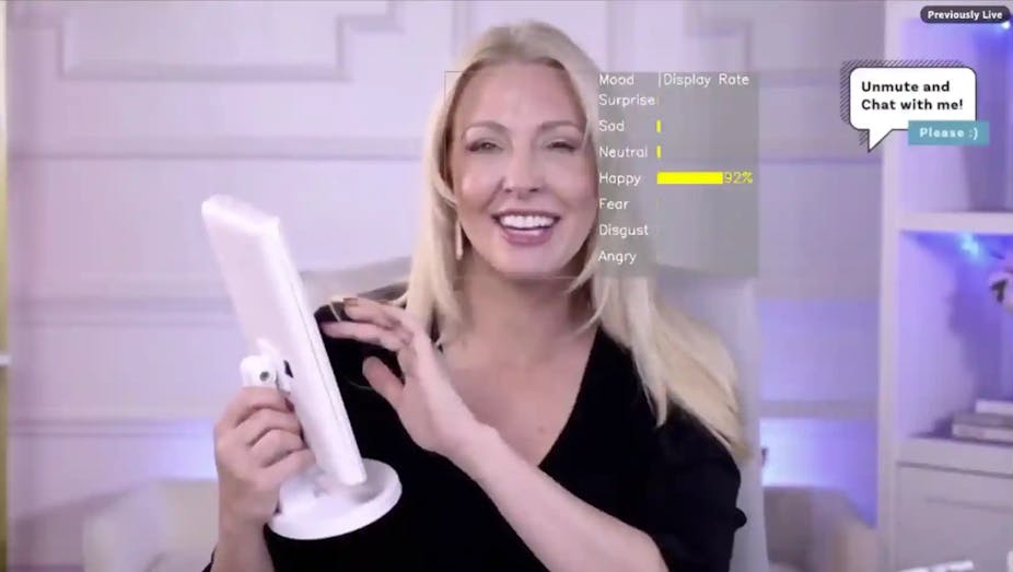 A woman smiles as she holds a screen and prepares to touch it with her other hand. A heads up display is overlaid near her face with the emotion of 'happy' highlighted.