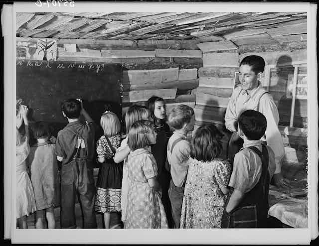 A teacher talking with students in a ramshackle one-room schoolhouse in 1940.