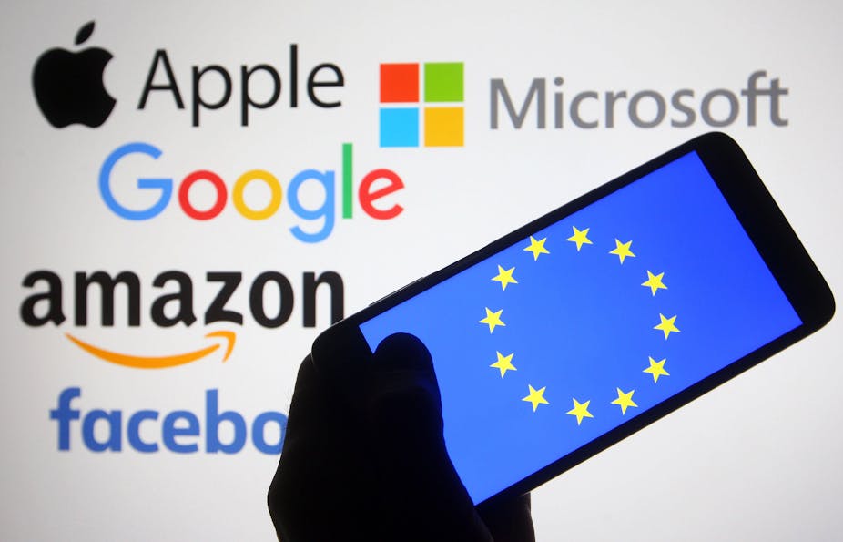 Silhouette of hand holding smartphone with EU logo with logos of big US tech companies in the background