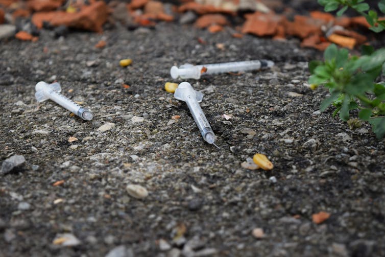 Used drug syringes on the pavement outdoors.