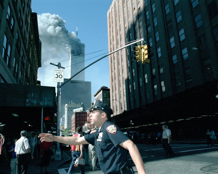 Police officer directing traffic in New York while World Trade Center burns after two planes crash into the twin towers