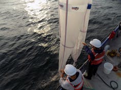 Two people lower conical nets off a research ship into the water.