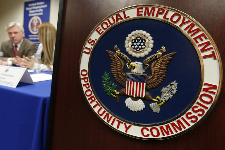 The U.S. Equal Employment Opportunity Commission seal is displayed in the foreground as a man and a woman chat at a table with a blue cloth draped over it.