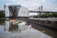 Large barge with conveyor belt pulling plastic debris out of river.