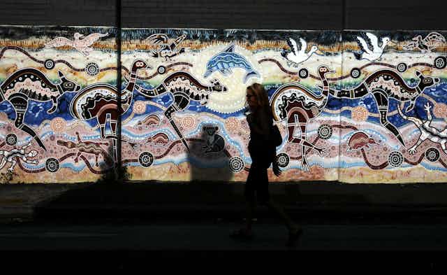 A woman passes an Aboriginal styled mural on a wall in Newtown, Sydney.
