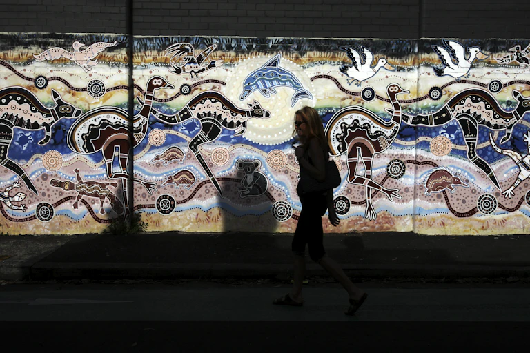 A woman passes an Aboriginal styled mural on a wall in Newtown, Sydney.