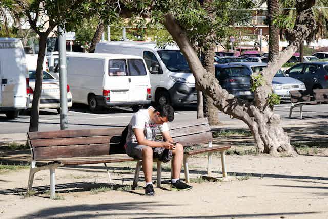 Un joven solo en el banco de un parque mirando el teléfono móvil.