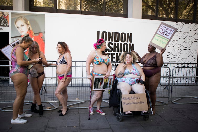 Women with diverse bodies wear bikinis and hold signs that read 'fashion for every body' and 'We want diversity on our runways.'