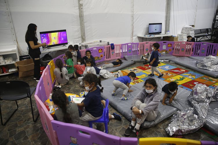 Young children watch TV inside a pen in the federal government's holding facility in Donna, Texas.