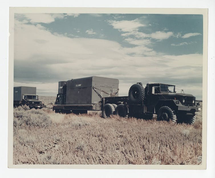 An army truck with a box on a trailer behind it