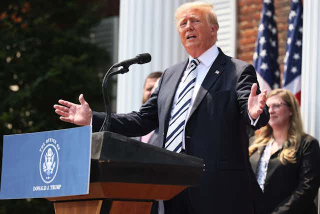 Donald Trump at a lectern speaking into a microphone and gesturing with his hands.