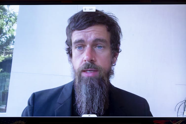 O CEO do Twitter, Jack Dorsey, um homem com olhos azuis brilhantes, cabelo castanho e uma barba rala de hipster, falando em um monitor.