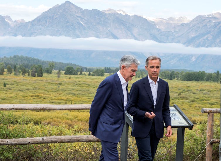 Jerome Powell and Mark Carney talk at a conference at Jackson Hole, Wyoming, with mountains behind them.
