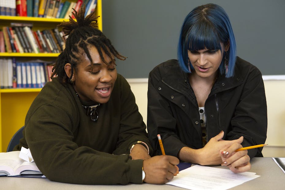 One young person is helping another with their school work in a library setting.