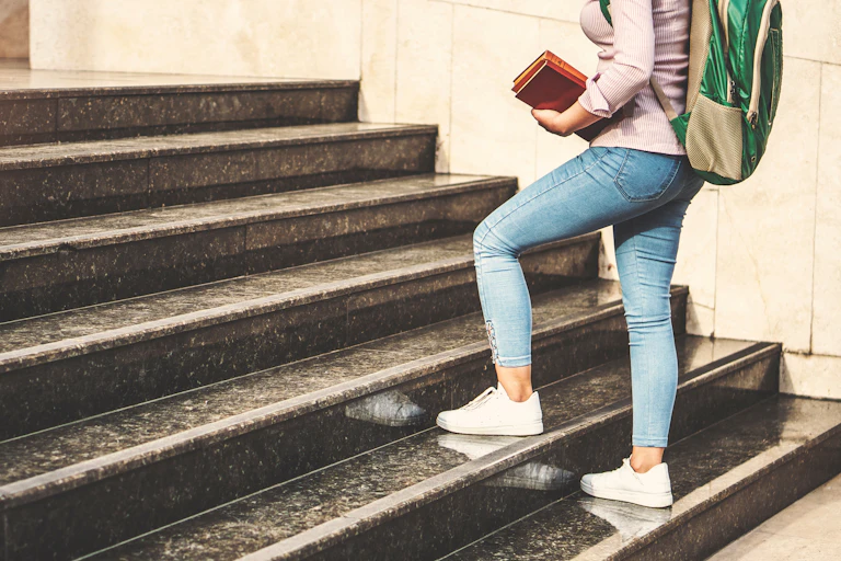 Feet with white sneakers seen paused on steps as a person mounts stairs.