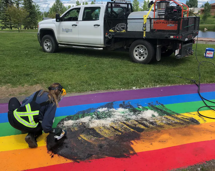 A worker cleans a rainbow path on the ground that has been vandalized.