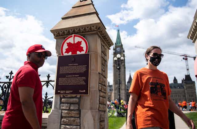 A man in red shirt stands in front of upside down maple leaf next to woman in orange shirt.