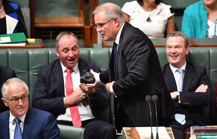 surprised man seated, other man standing holding piece of coal