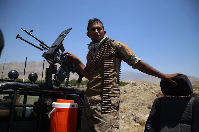 An Afghan soldier manning an armoured vehicle with a bandoleer of ammunition around his neck.