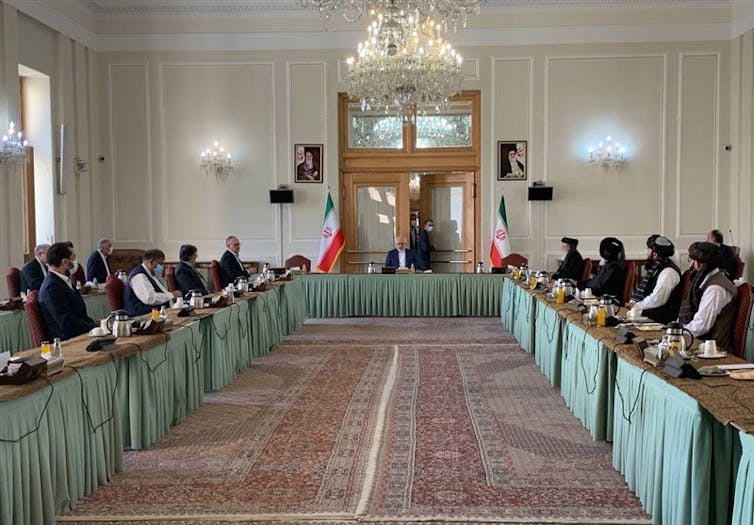 Afghanistan government officials and representative of the Taliban sit at long tables in a conference room in Tehran.