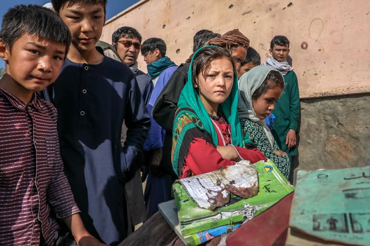 Yojg girls and boys with bloodstained school books and belongings of pupils killed in a car bomb attack on a Kabul high school, May 2021.