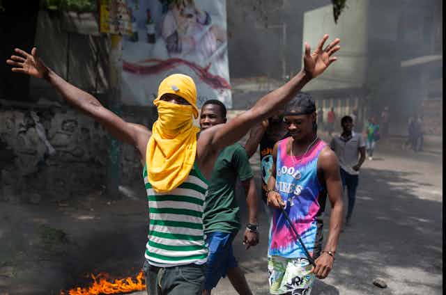 Jeunes hommes manifestant dans une rue, l'un d'eux masqué