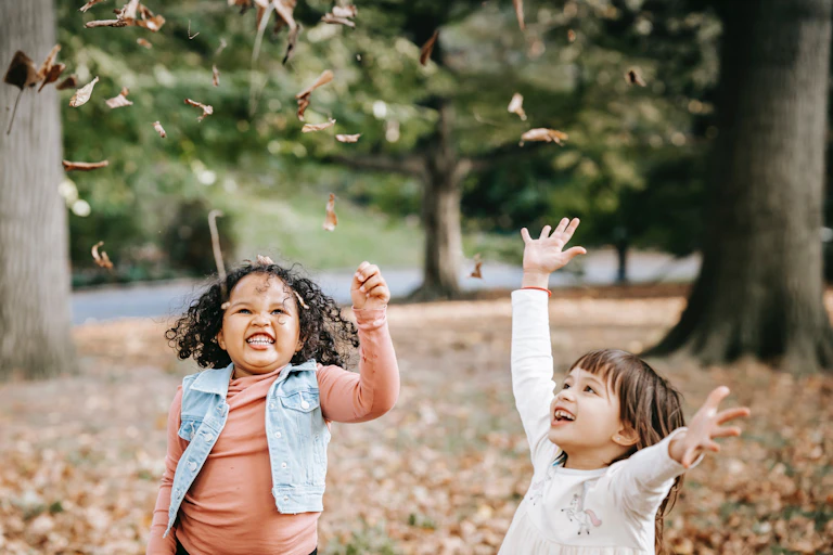 Two children throwing leaves in the air.