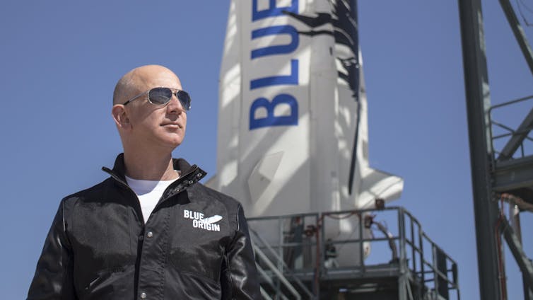 Jeff Bezos wearing sunglasses and standing in front of a Blue Origin rocket.