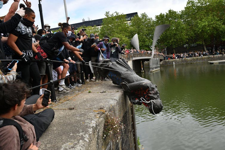Protestors throw a statue into a river.