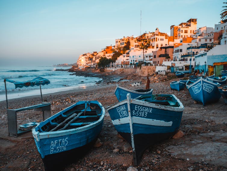Traditional fishing boats line a beach in a coastal village in Morocco.