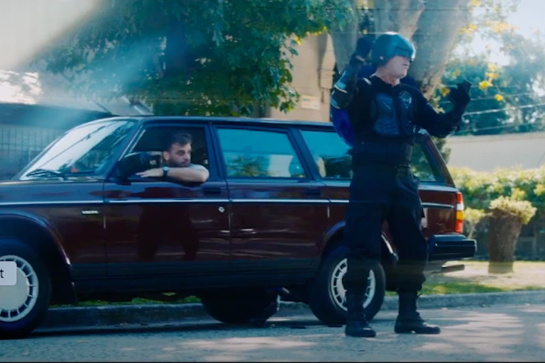 A man in a superhero outfit stands next to a car