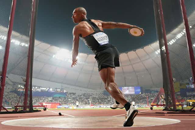 Full-body shot of an athlete in the middle of a discus throw with a full stadium in the background