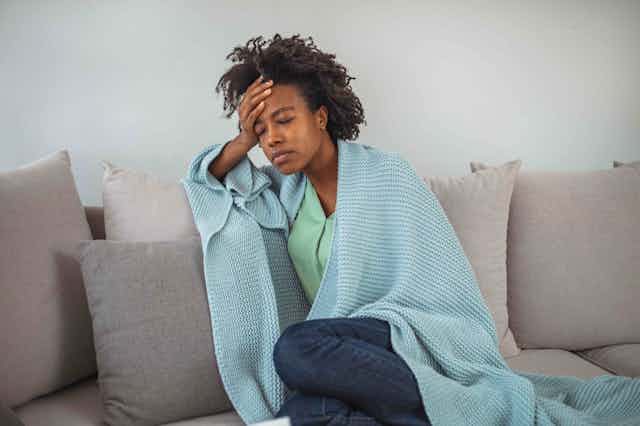 A woman sits on the couch wrapped in a blanket.