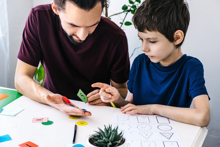 A man and a little boy sitting at a table working on number and shape exercises.