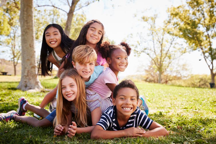 A group of children piled on top of each other in a park.