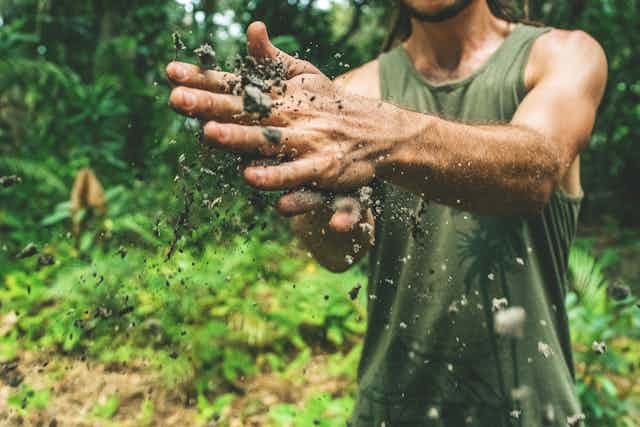 A person rubs their hands with soil