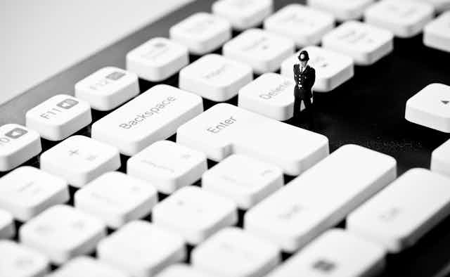 Miniature Police officer on top of computer keyboard.
