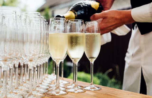 A waiter pours champagne into multiple champagne flutes