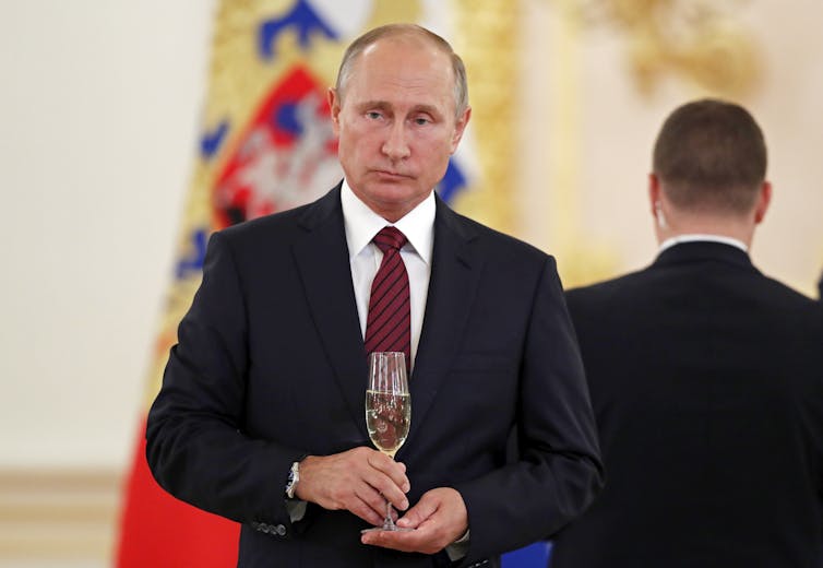 Russian President Vladimir Putin holding a glass of champagne at an event.