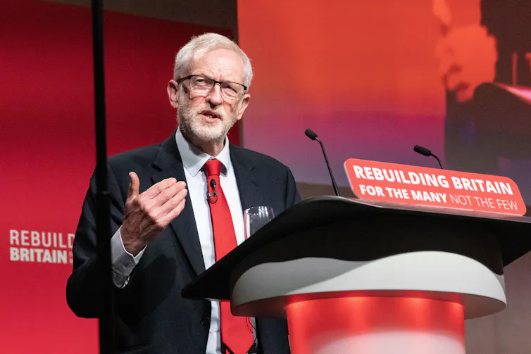 Former Labour leader Jeremy Corbyn giving a speech at a podium that reads Rebuilding Britain for the many, not the few.