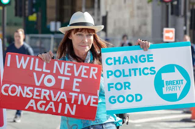 A woman holds two placards: One says "I will never vote conservative again," the other reads "Change politics for good: Brexit Party