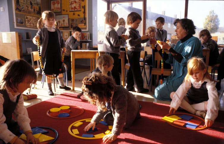 Primary school pupils play with coloured shapes on a red carpet
