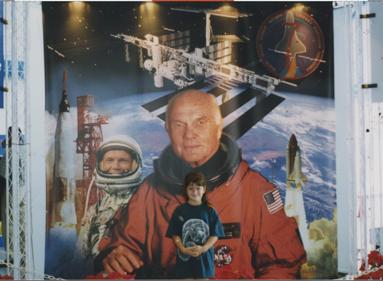 smiling girl stands in front of a John Glenn space mural